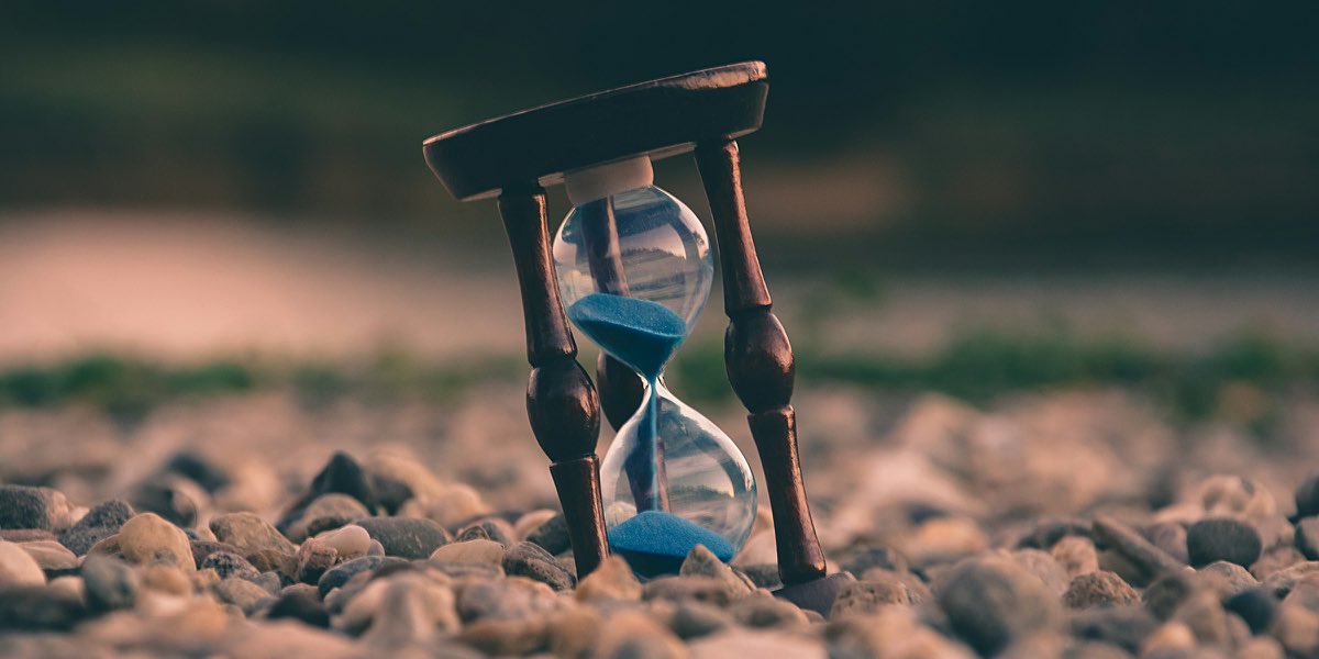 A small hourglass standing on pebbles, a little blue sand left in the top