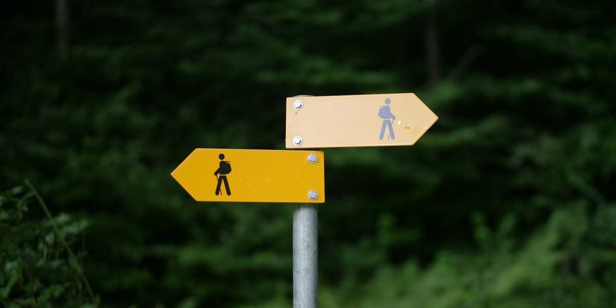 Two yellow hiking signs on one post, pointing in opposite directions