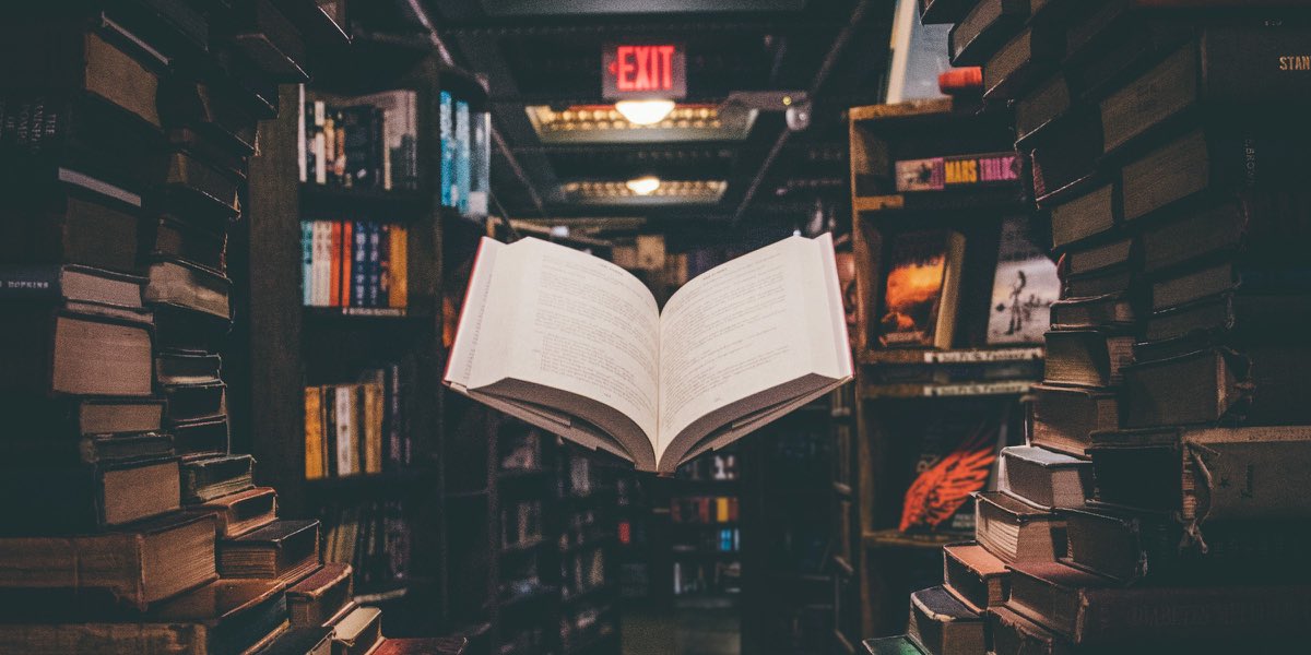 An open book floating above stacks of books in a library aisle