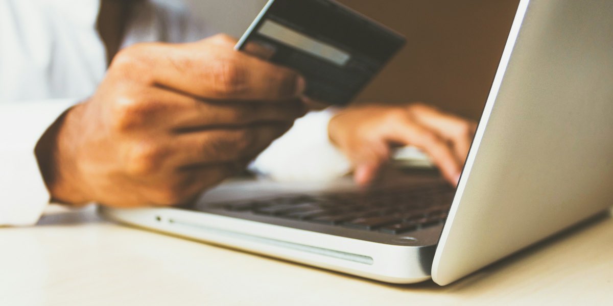 A hand holding a bank card above an open laptop